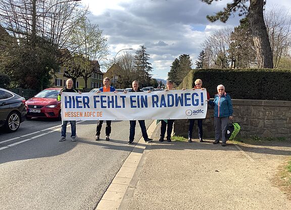 Personengruppe hält Banner hoch "Hier fehlt ein RAdweg"