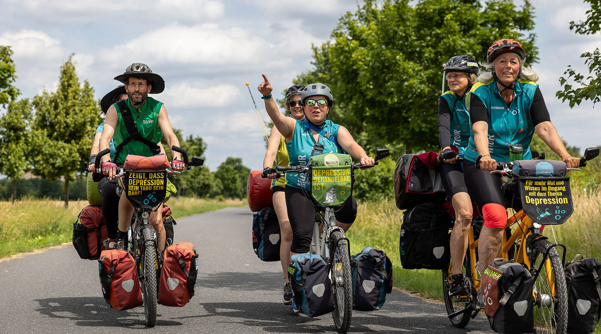 Drei Tandems mit Radfahrerinnen und Radfahrer radeln auf einer Landstraße.