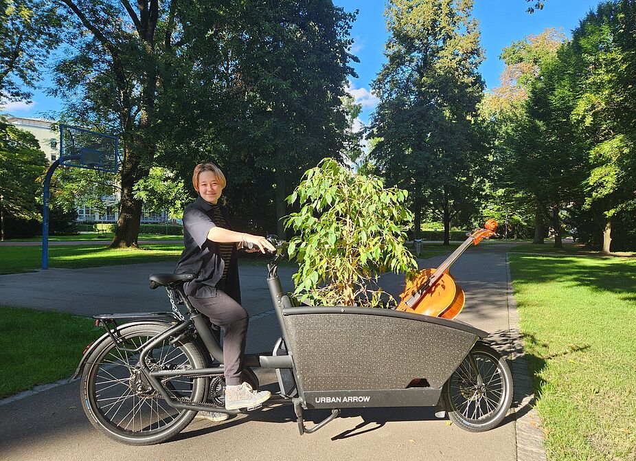 Ulf-Lastenrad mit Cello Eine Frau transportiert mit dem Lastenrad ein Cello und einen Ficus.