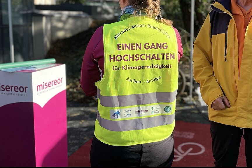 Mit dem Rad zur Klimakonferenz Einen Gang hochschalten steht auf der gelben Warnwete einer Radlerin zur Klimakonferenz