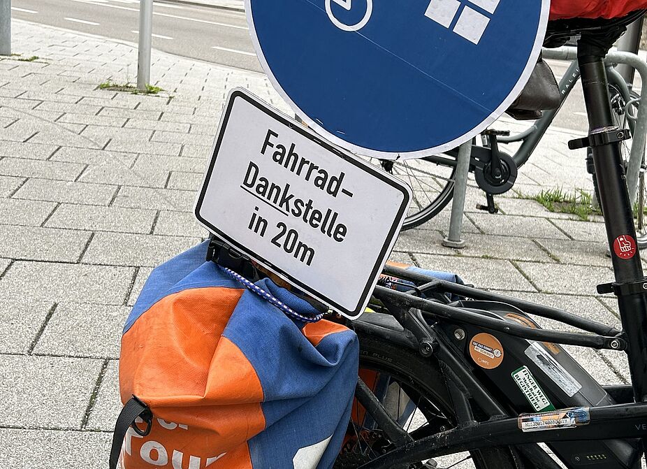 Schild zur Fahrrad-Dankstelle Ein Fahrrad mit einem Schild weist den Weg zur Dankstelle für die Radler und Radlerinnen.