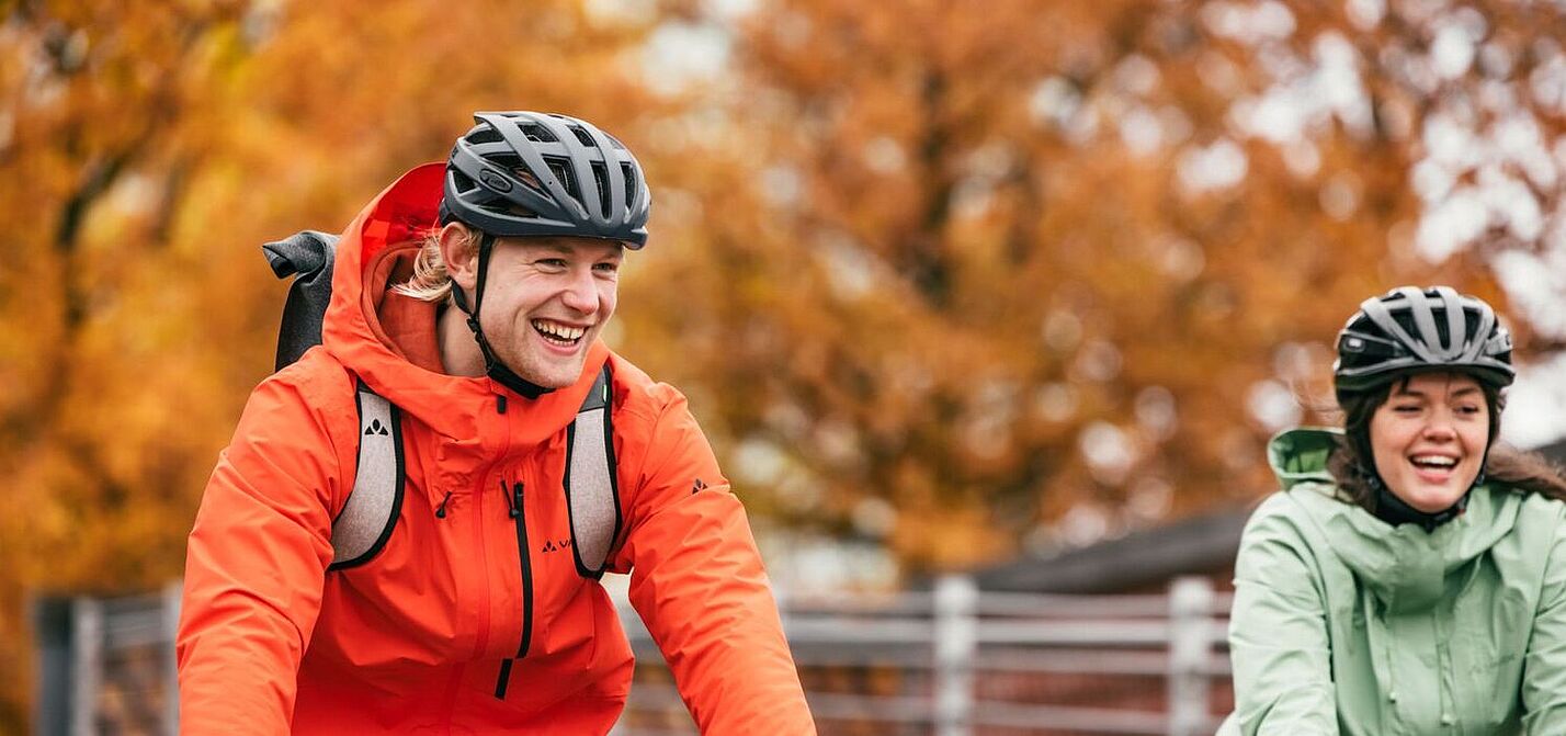 Radfahren im Herbst Eine Frau und ein Mann mit Fahrrädern von vorn in herbstlicher Kleidung lächlen in die Kamera.